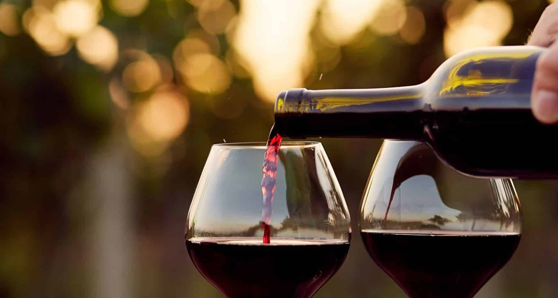 A close-up of Paraguay wine being poured from a bottle into one of two wine glasses, with a blurred outdoor background and warm evening light—perfect for food tours or pairing with delicious Paraguay food.