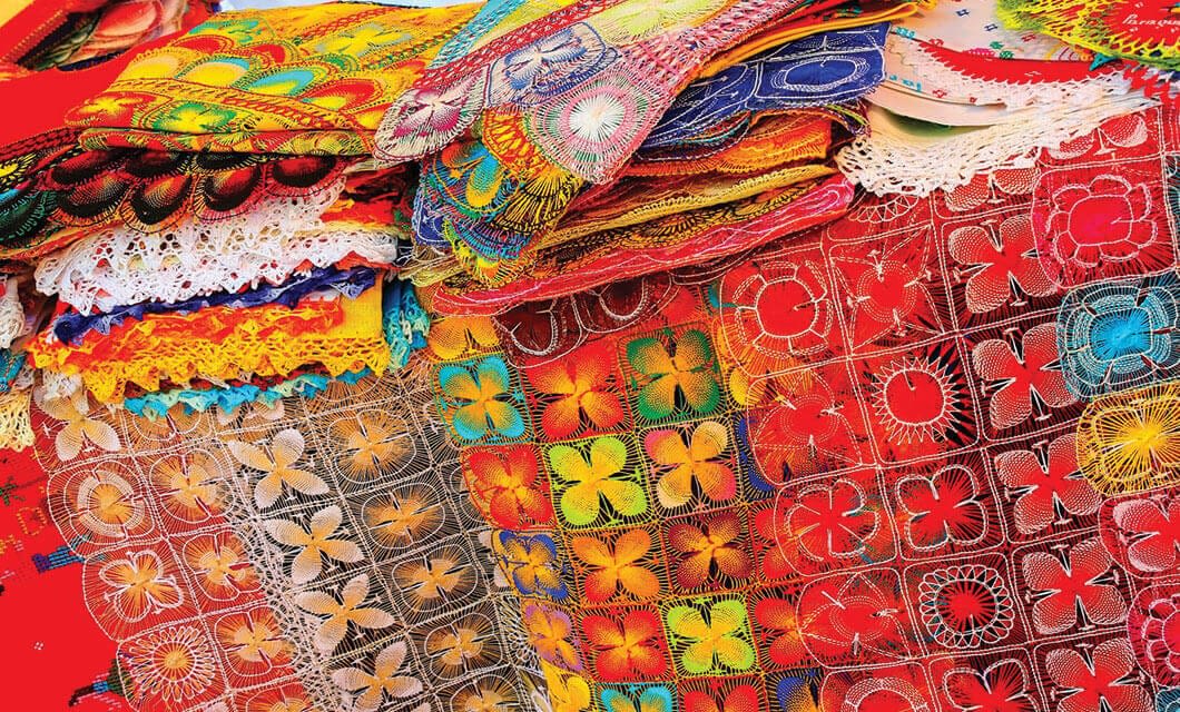 Stacks of vibrant, colorful embroidered textiles with intricate patterns and lace edges, featuring traditional Paraguayan designs—an eye-catching highlight for anyone exploring Paraguay travel or seeking unique things to do in Paraguay.