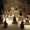 Small ceramic figurines and vessels from South America are displayed on white pedestals in a museum exhibit. The objects, arranged in rows under soft lighting, highlight the artistry that makes any trip or travel to this region unforgettable.
