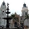 Historic cathedral in Peru with two towers and a large, ornate black fountain in the foreground; palm trees and arched doorways are visible under a cloudy sky, making it perfect for your greatest holiday.
