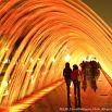 People enjoy a nighttime trip through a glowing tunnel made of curved orange and yellow lights, creating a vibrant, illuminated pathway.