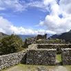 Ancient stone ruins surrounded by green hills and mountains under a blue sky with scattered clouds—a breathtaking scene perfect for any trip to Peru.