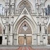 The image shows the ornate entrance of a Gothic-style cathedral featuring pointed arches, detailed stone carvings, and three large wooden doors—perfect for visitors hoping to have a fabulous time exploring its historic beauty.