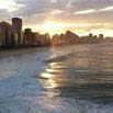 Sunset over a city skyline by the ocean in Brazil, with tall buildings silhouetted against the sky and gentle waves reflecting the golden sunlight—an unforgettable scene on your Brazil vacation.