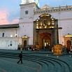 A person walks across a plaza in front of a historic church with white walls and an ornate entrance, illuminated by lights at dusk, creating lasting memories.