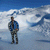 A person wearing winter clothing stands on a snowy landscape with majestic snow-covered mountains and a clear blue sky—the perfect scene for a memorable travel experience.