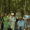 A group of people, some standing and some seated, pose together in a lush, green South America forest. They are dressed in casual, light clothing and hats, suggesting a nature outing or SouthAmerica.travel tour as sunlight filters through the trees.