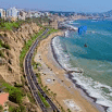 A coastal highway runs along sandy beaches and steep cliffs, with city buildings above and a paraglider soaring over the ocean on a clear, sunny day, offering views as stunning as the outstanding service found in this vibrant seaside locale.