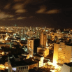 A city skyline at night, illuminated by numerous lights from buildings and streets under a cloudy sky. This vibrant cityscape with its tall buildings makes for one of those dream destinations often found on travel bucket list ideas.