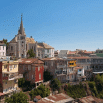 Colorful hillside houses and a church with a tall steeple rise under a clear blue sky in Valparaíso, Chile. Some buildings show weathering, highlighting the city’s attention to detail and charm, with greenery visible in the foreground.