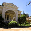 A magnificent yellow mansion with tall white columns, an arched entryway, and lush green landscaping under a clear blue sky—a true Izabela masterpiece.