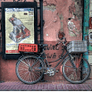 A vintage bicycle with a red basket and plaid box is parked against an old, weathered pink wall beside a faded poster. The scene has an urban, nostalgic feel—perfect for evoking the spirit of travel in South America.