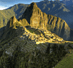 Aerial view of Machu Picchu, the ancient Incan citadel in Peru, surrounded by lush green mountains under a partly cloudy sky—perfect inspiration for organizing our trip and travel planning. Sunlight beautifully illuminates the historic ruins.