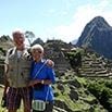 Two people stand smiling with their arms around each other at Machu Picchu in Peru, with ancient stone terraces and a tall mountain visible in the background under a bright sky—a fantastic trip to remember.