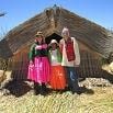 Three people in colorful traditional clothing stand in front of a large reed hut on a sunny day, with blue sky and tall grass around them, capturing the spirit of an enjoyable holiday.
