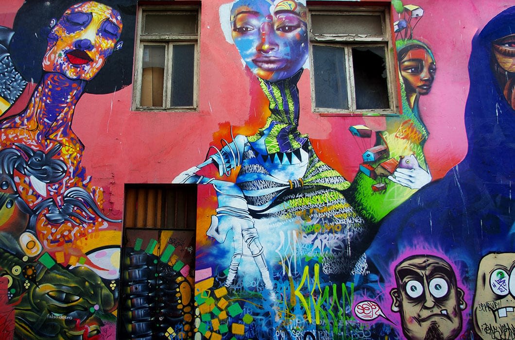 Colorful street mural featuring abstract faces, a large central figure with blue and purple hues, two windows above, and surreal elements on a bright red wall—a must-see Chile attraction for anyone interested in art and unique things to do in Chile.