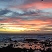 Colorful sunset over the ocean, with dark rocky shore in the foreground and vibrant clouds in shades of pink, orange, and blue—a tranquil scene that reflects the excellence of superb services.