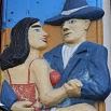 A colorful relief sculpture shows a woman in a red dress and a man in a blue suit and hat dancing closely together, gazing at each other and smiling, evoking the joy of an excellent trip filled with unforgettable moments.