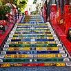 Colorfully painted outdoor staircase with each step featuring vibrant, artistic designs and patterns. Red railings border the stairs, perfect for a last minute travel photo op as sunlight illuminates the lively scene from the top of the stairs.