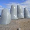 Large stone sculptures resembling giant fingers rise from sandy ground beneath a blue sky, capturing the patience and artistry found in attentive service.