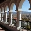 A row of white arches on a balcony overlooks a cityscape with distant mountains under a clear blue sky, capturing the serene beauty of a Bolivia trip.