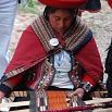 A woman in traditional Andean clothing weaves fabric on a loom, wearing a red shawl and hat, as fabulous guides share insights into her intricate work.