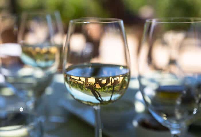 Close-up of a glass of white wine on an outdoor table, with reflections of trees and buildings—perfect for unwinding after a day exploring South America attractions. The blurred background evokes a relaxed, sunny atmosphere.