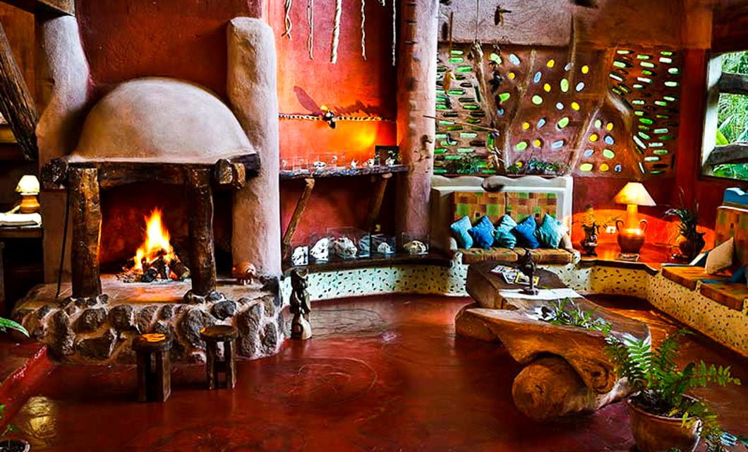 Colorful, rustic living room inspired by Argentina’s Yacutinga Lodge, with a lit fireplace, organic-shaped furniture, wooden accents, and vibrant cushions. Soft lighting, plants, and decorative walls create a cozy, artistic atmosphere.