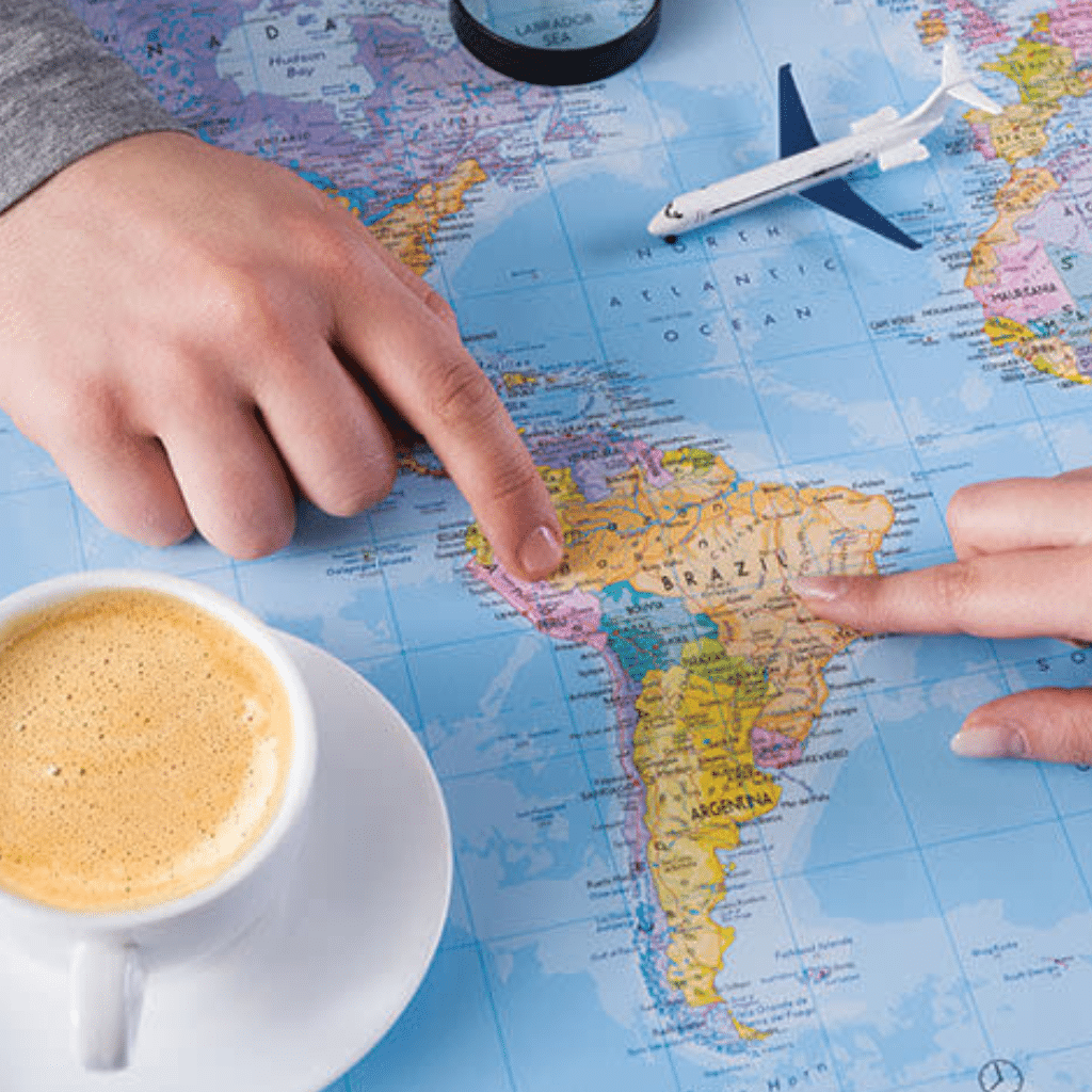 Two hands point to Brazil on a world map beside a small toy airplane. A cup of coffee sits nearby, inspiring you to book with confidence as you plan your adventure to South America.