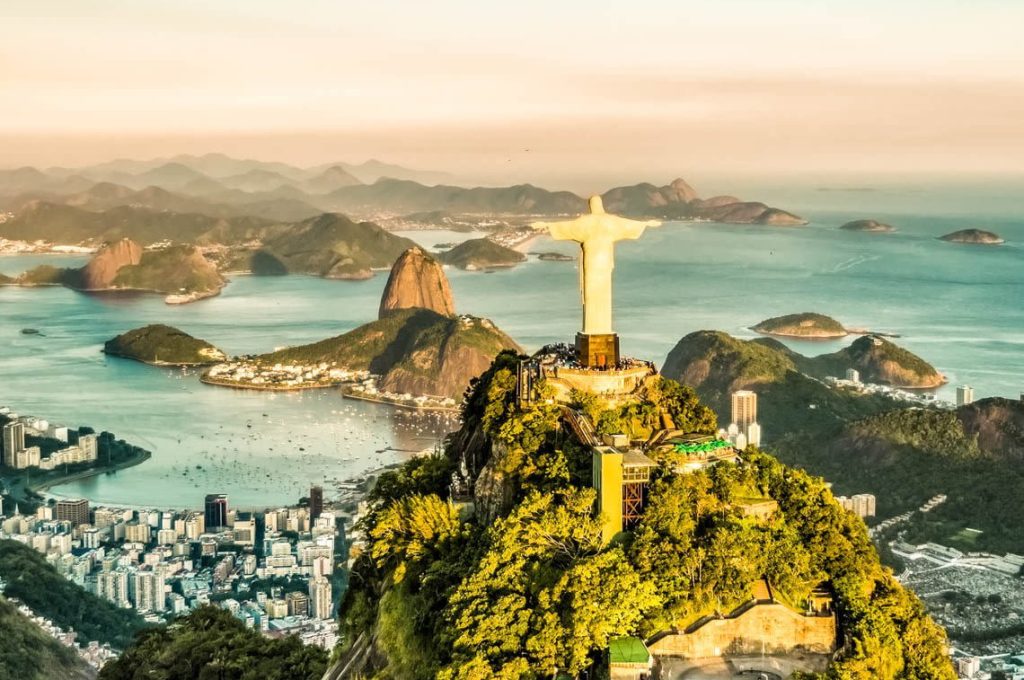 Aerial view of the Christ the Redeemer statue atop Corcovado Mountain, overlooking Rio de Janeiro—one of the top reasons to visit Brazil—with Sugarloaf Mountain and the ocean in the background under a clear sky.
