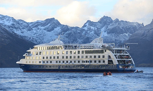 A cruise ship sails through the water with gorgeous mountains in the background