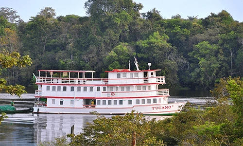 The Tucano River Cruise sails through the river, with lush trees surrounding