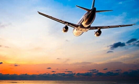Airplane flies over ocean at sunset