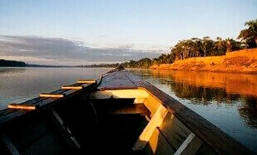 Prow of canoe moves down river at sunset