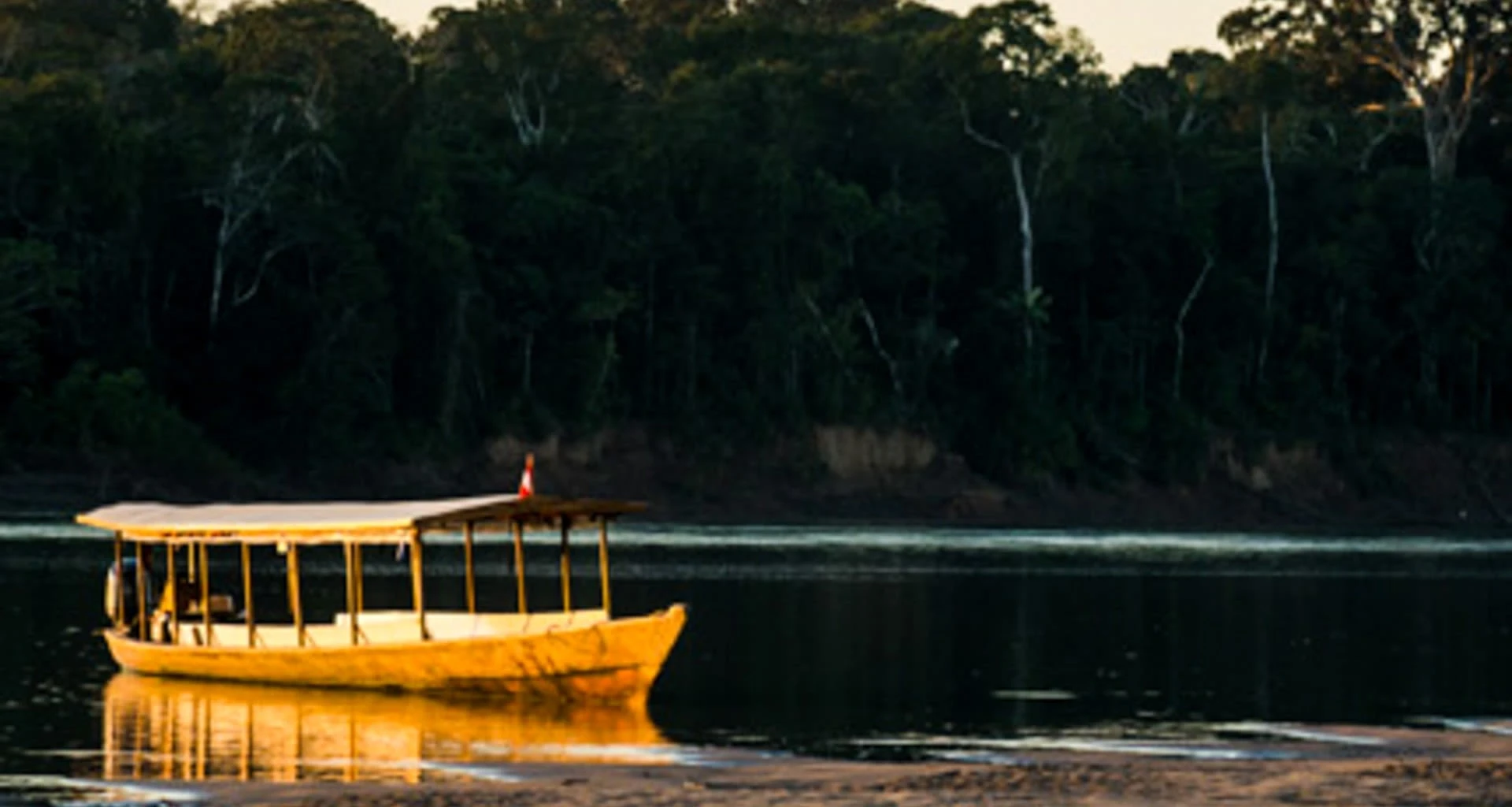 Covered boat sits on beach of river
