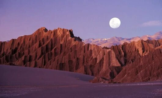 Full moon hangs above desert peaks