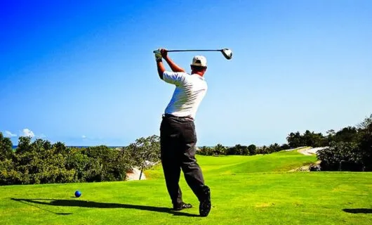Golfer swings club on sunny golf green