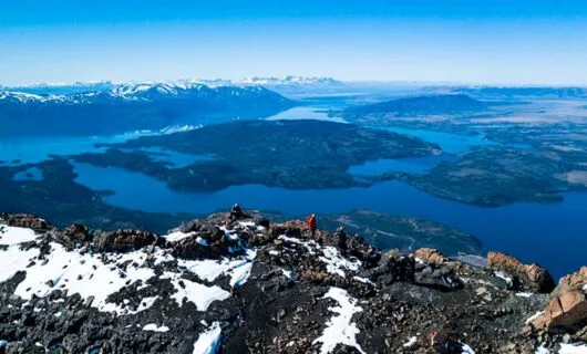 Hikers rest on top of of ridge overlooking lake valley