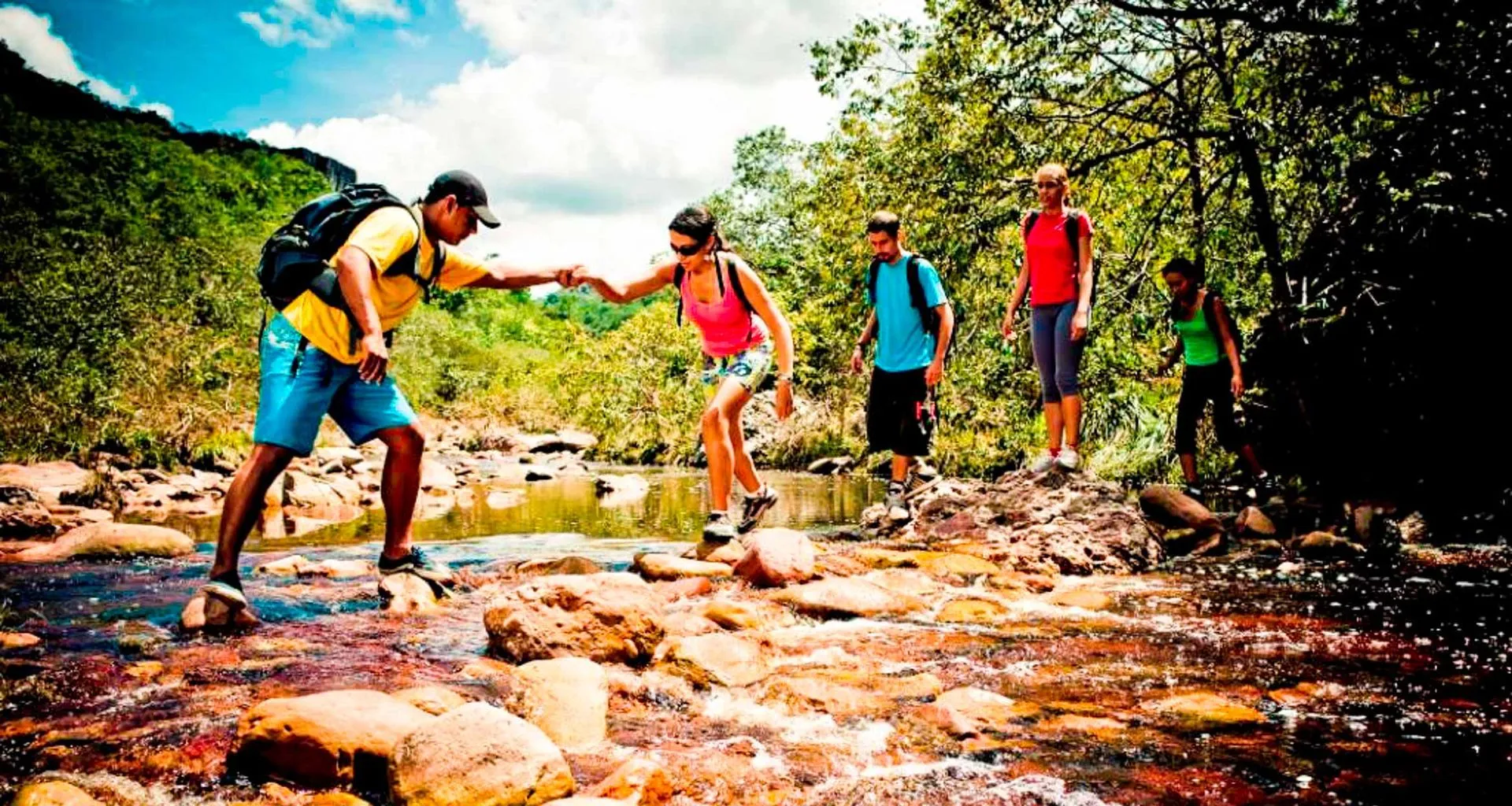 Hikers help each other across rocky stream
