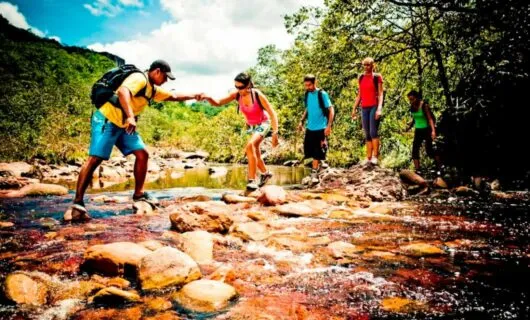 Hikers help each other across rocky stream