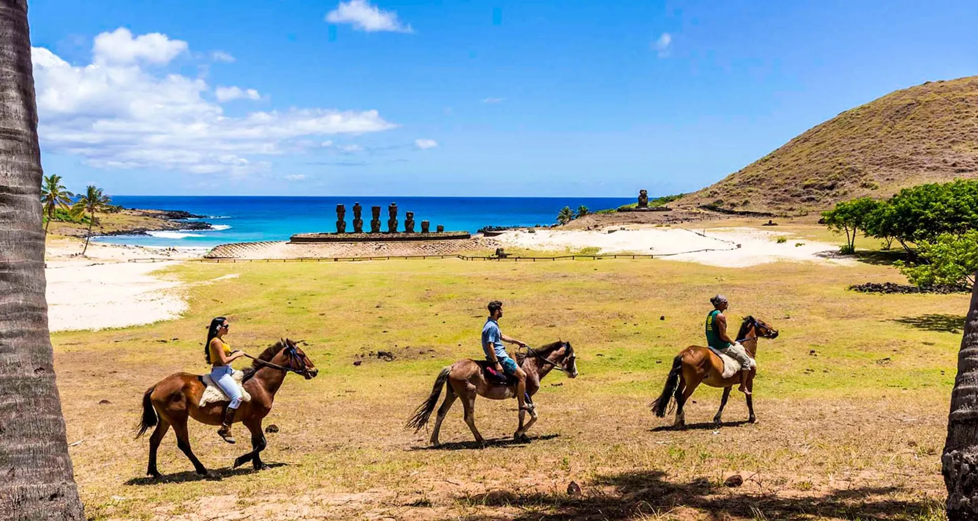 Travelers ride horses along beach near row of stuatues