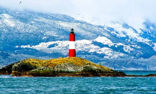 Red and white lighthouse on island near mountains