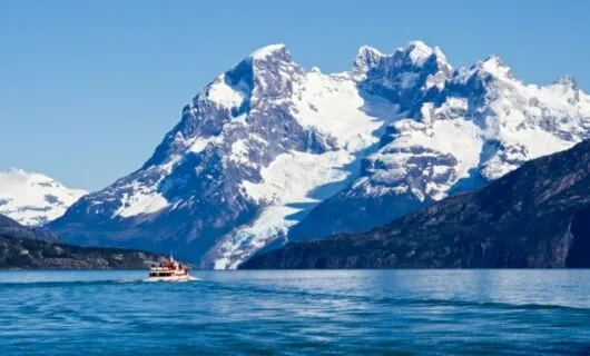 Motorboat drives across lake in front of mountains