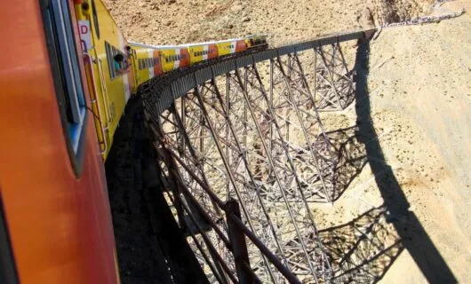 Orange and yellow train runs along railway bridge