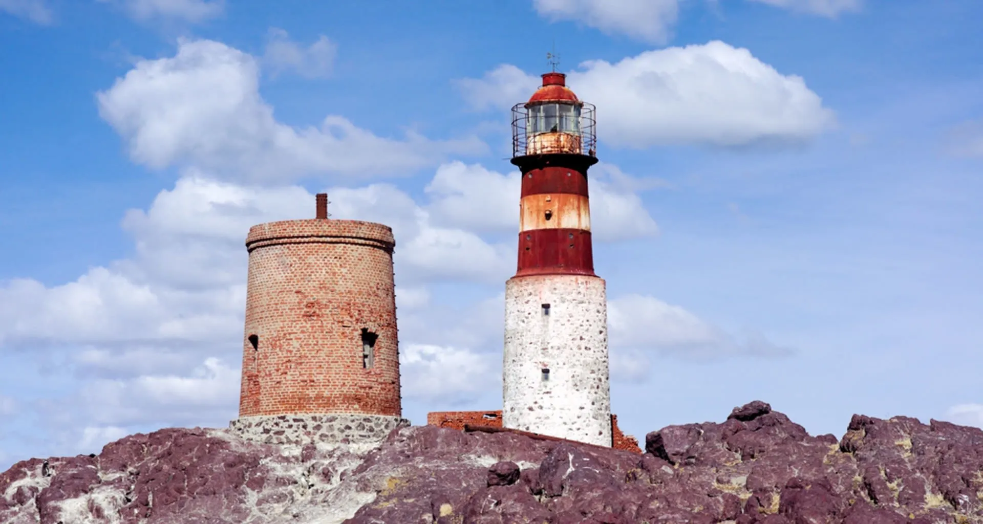 Red and white striped lighthouse on red rocks
