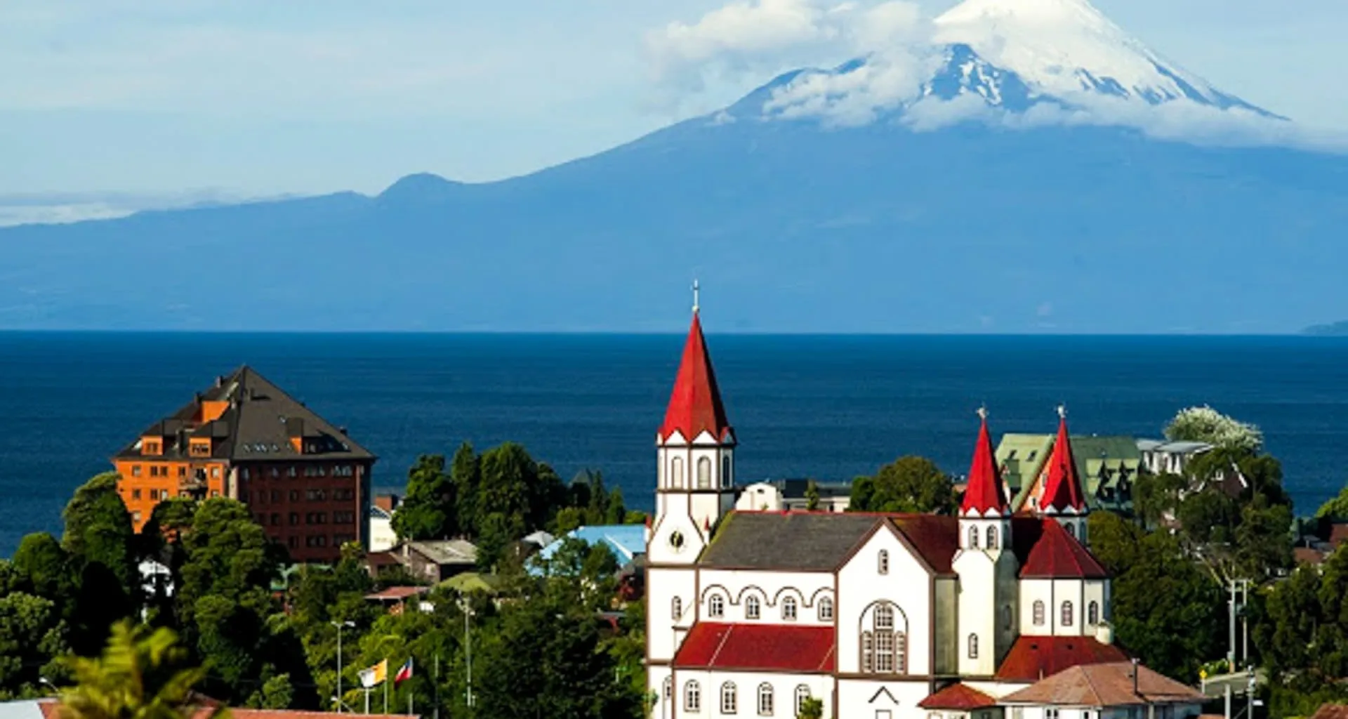 Red-roofed church in front of lake and mountain