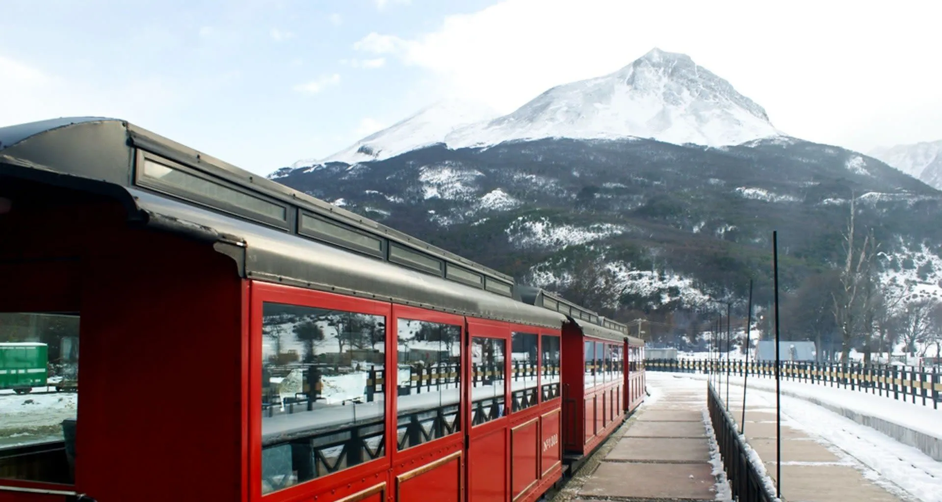 Red train sits on railway in front of mountain