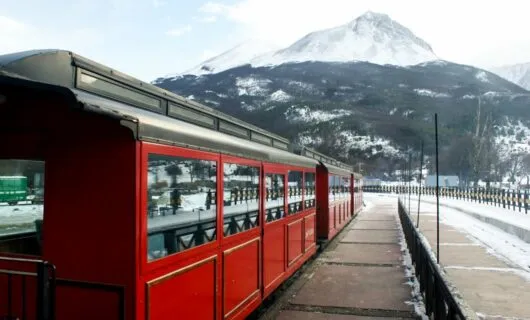 Red train sits on railway in front of mountain