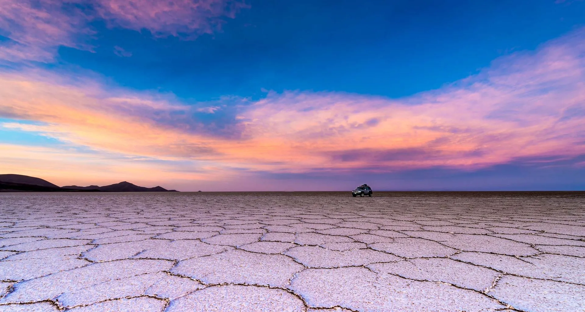 SUV rests on Bolivia salt flats at sunset