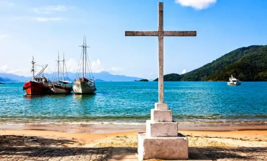 Cross stands on shore with boats in background
